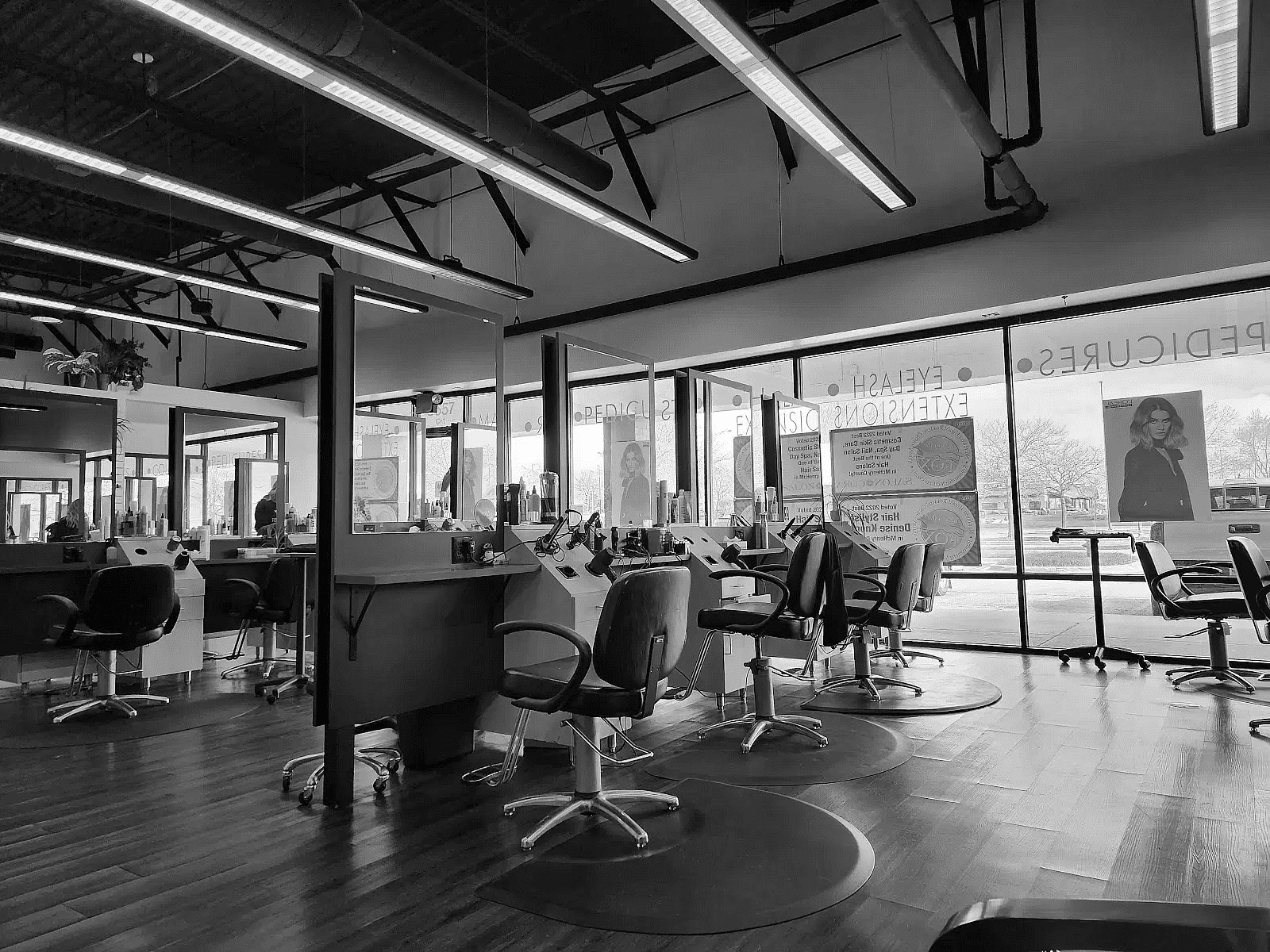 Empty salon chairs and stations, sleek modern salon interior with large windows and natural light.